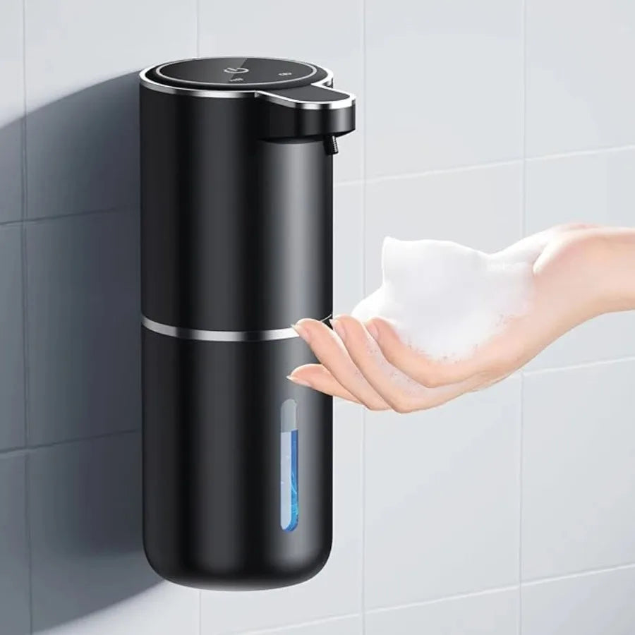 Black soap dispenser on a tiled wall with a hand reaching out for soap.