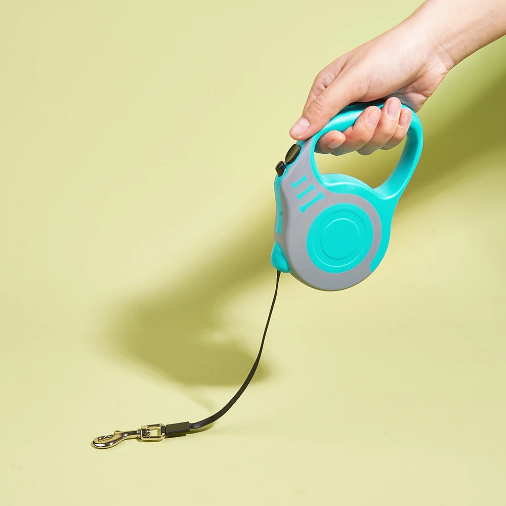 Turquoise and gray retractable dog leash with a hand holding it on a light yellow background