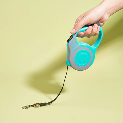 Turquoise and gray retractable dog leash with a hand holding it on a light yellow background