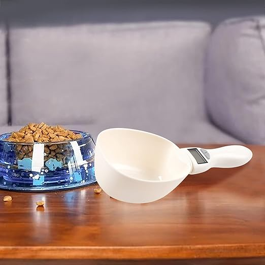 White pet scoop next to a blue pet bowl filled with kibble on a wooden surface.