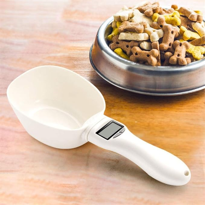 White pet food scoop with digital scale next to a metal bowl of dog food on a wooden surface